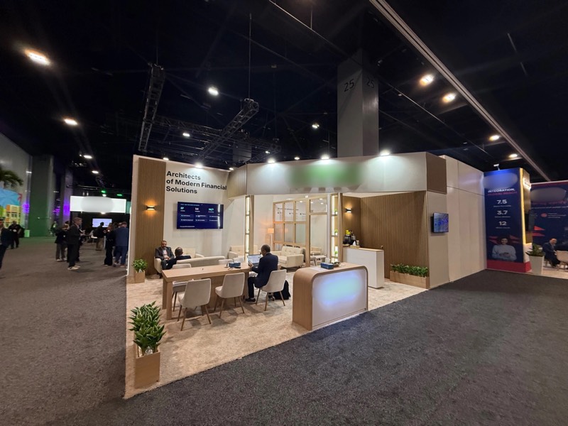Wide view of the wood slat exhibition stand with meeting table, reception counter and LED screen at SIBOS 2026